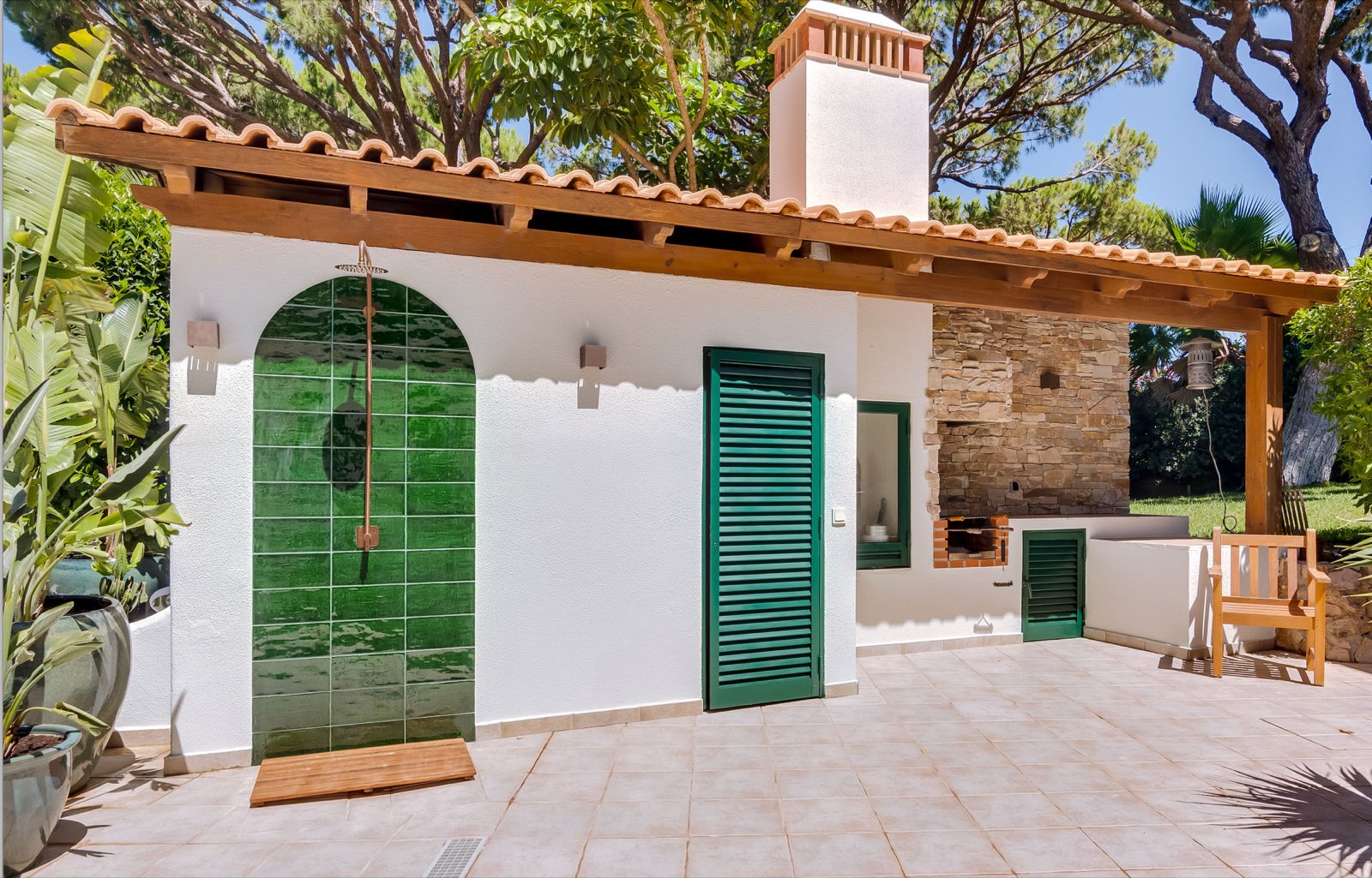 Pool house with green-tiled outdoor shower, stone BBQ fireplace and flowering garden at Casa da Fortuna